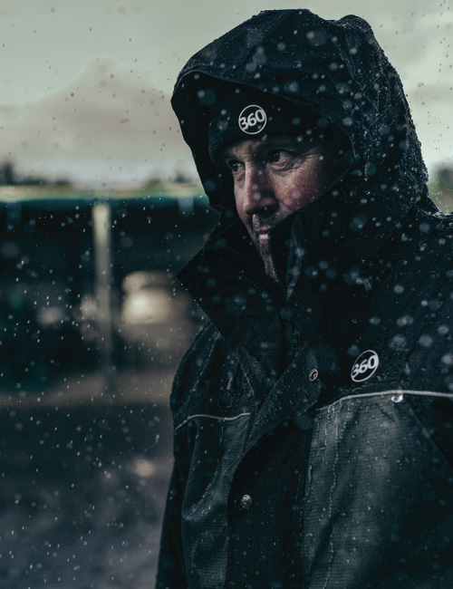 Man wearing 360 jacket and beanie covered in rain droplets